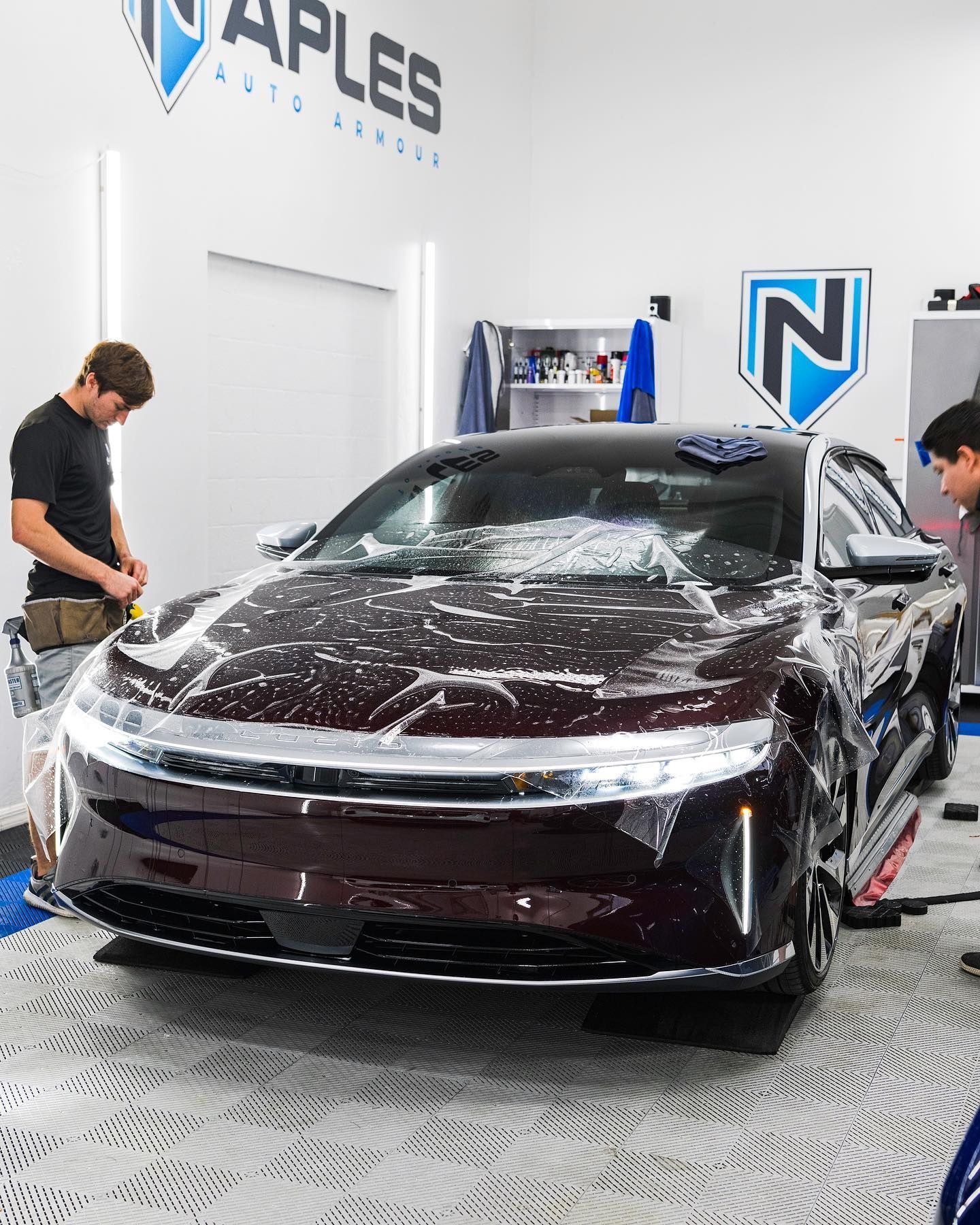 Black sedan being detailed in a car shop, with soap suds on the hood and two workers nearby