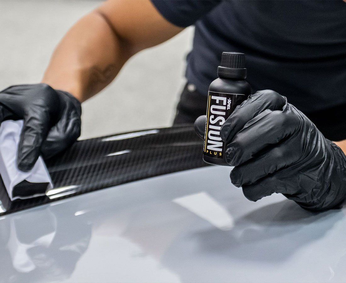 A person wearing black gloves is holding a bottle of fusion