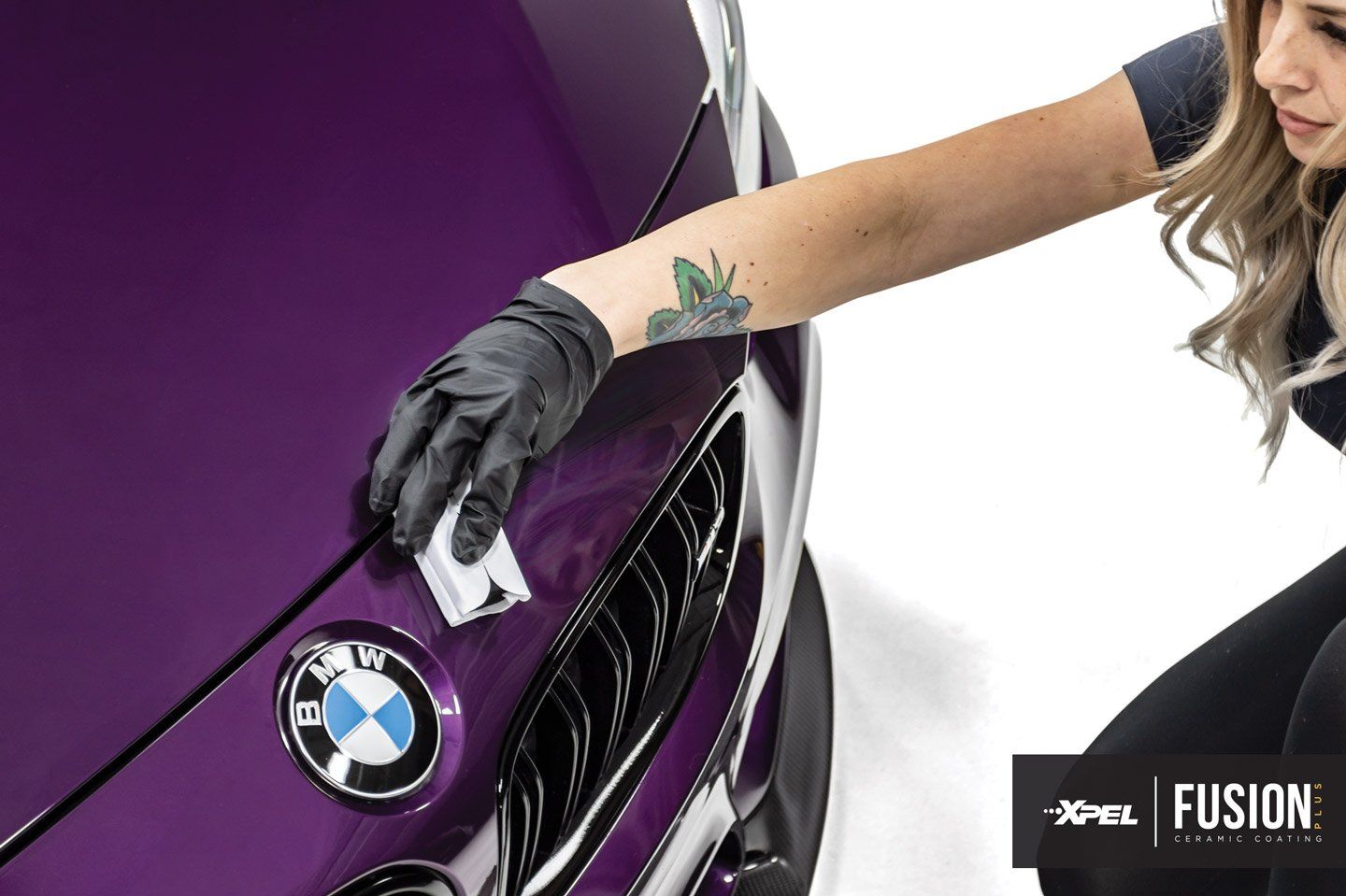 A woman is polishing the hood of a purple bmw.