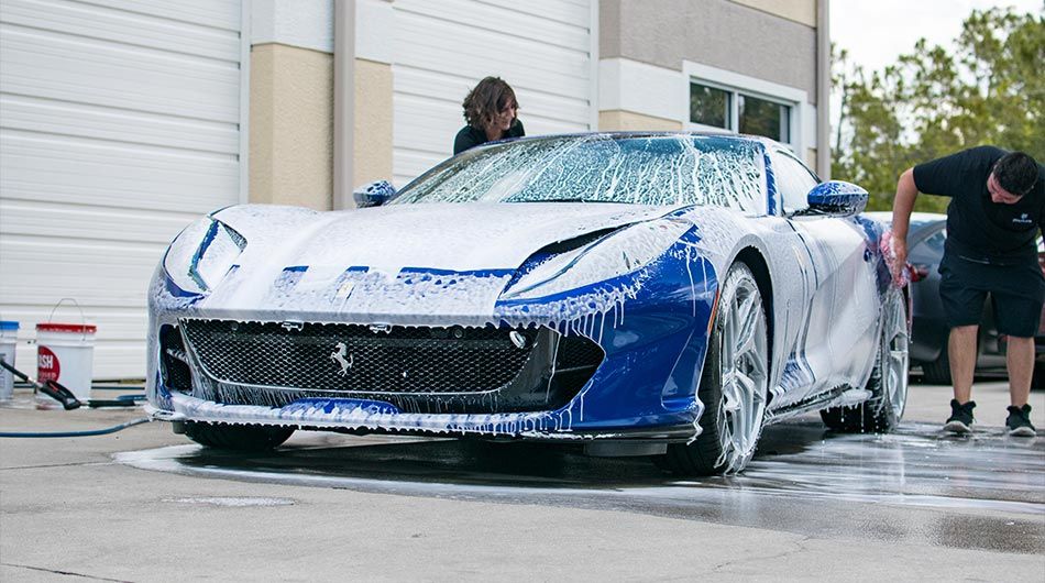A man is washing a blue and white sports car with foam.