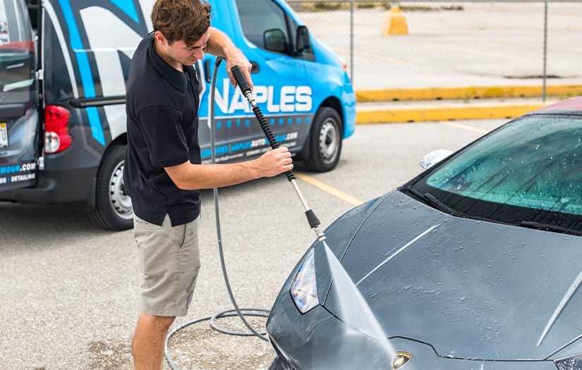 A man is washing a car with a high pressure washer in a parking lot.