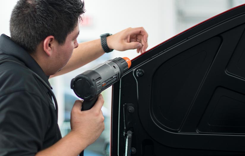 A man is working on a car with a drill.