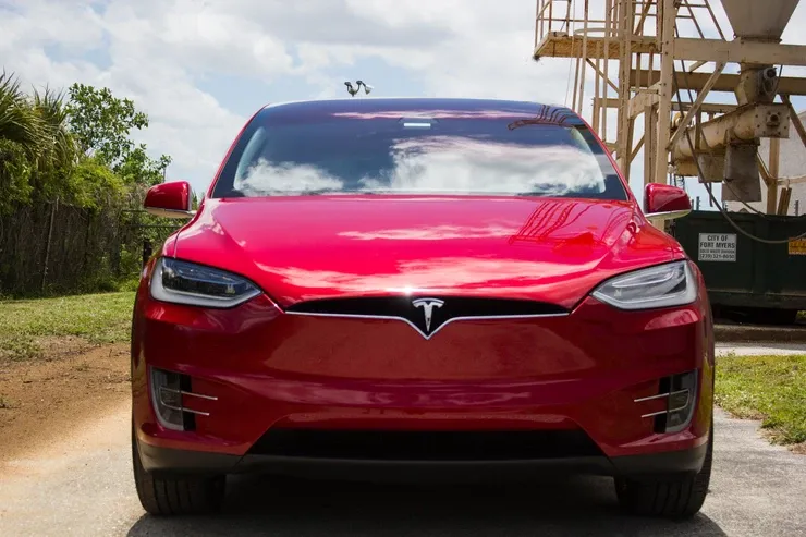 A red tesla model x is parked in a driveway.