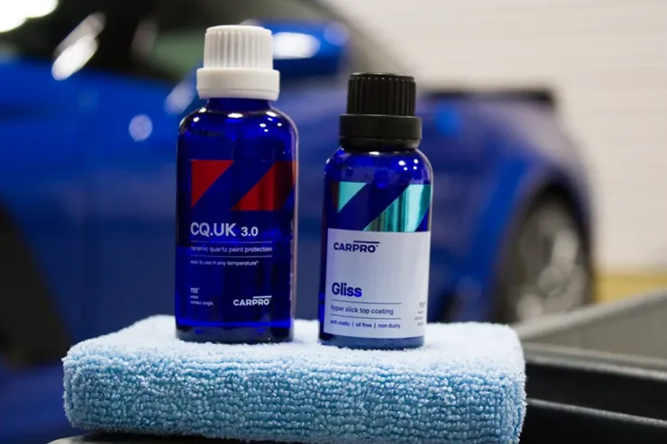 Two blue bottles are sitting on a blue towel in front of a blue car.