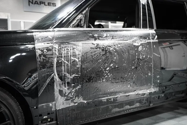 A black range rover is covered in clear plastic.