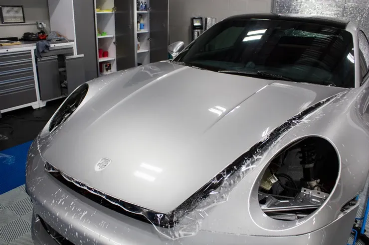 A silver porsche is wrapped in plastic in a garage.