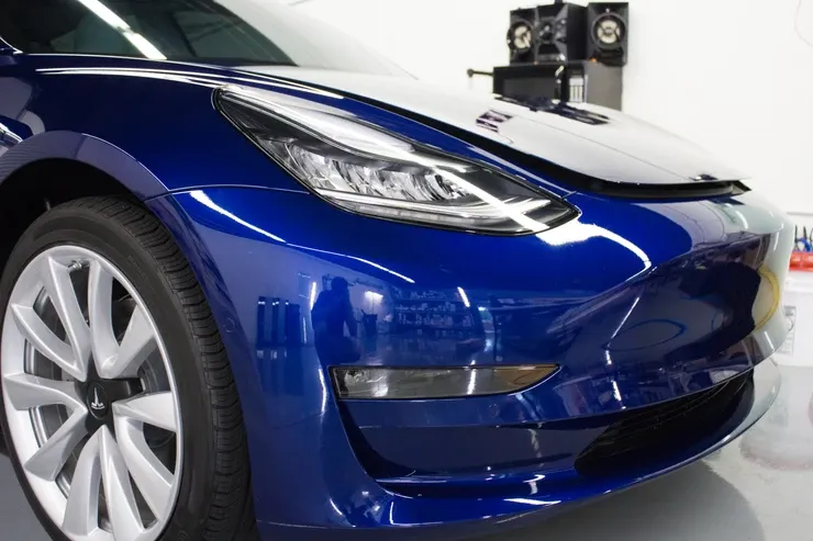 A blue tesla model 3 is parked in a garage.