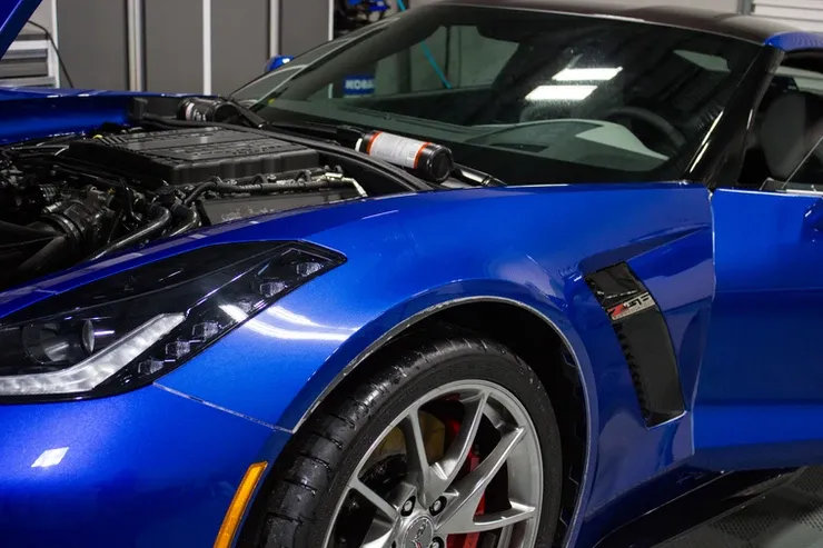 A blue sports car with the hood open is parked in a garage.