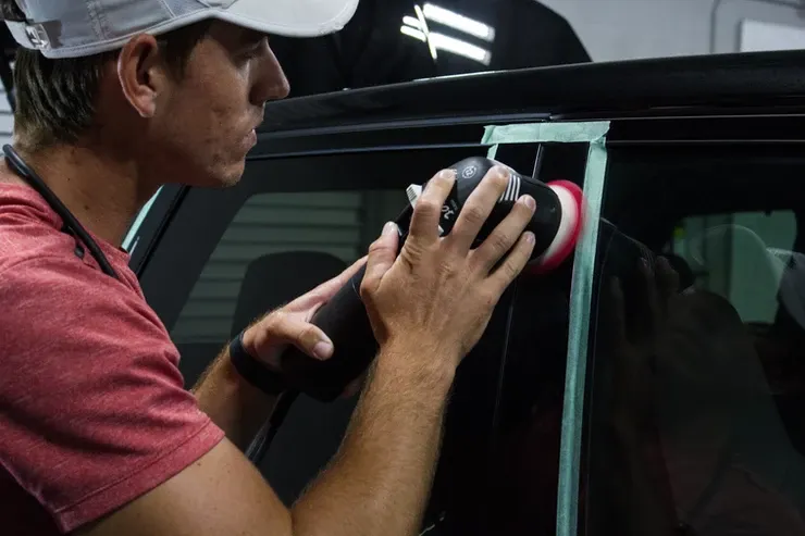 A man is polishing a car window with a machine.