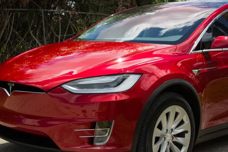 A red tesla model x is parked on the side of the road.