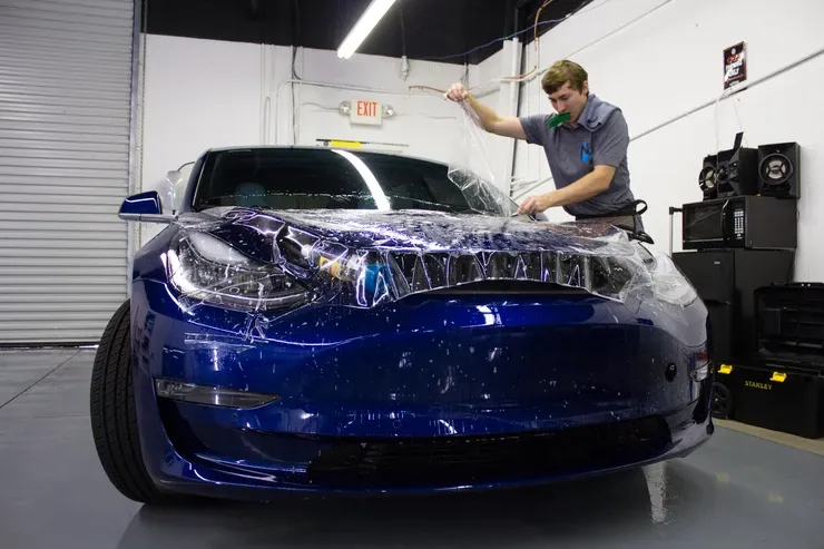 A man is wrapping a blue tesla model 3 in plastic.