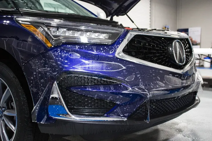 The front of a blue acura integra is covered in protective film.