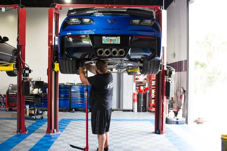 A man is working on a blue car on a lift in a garage.