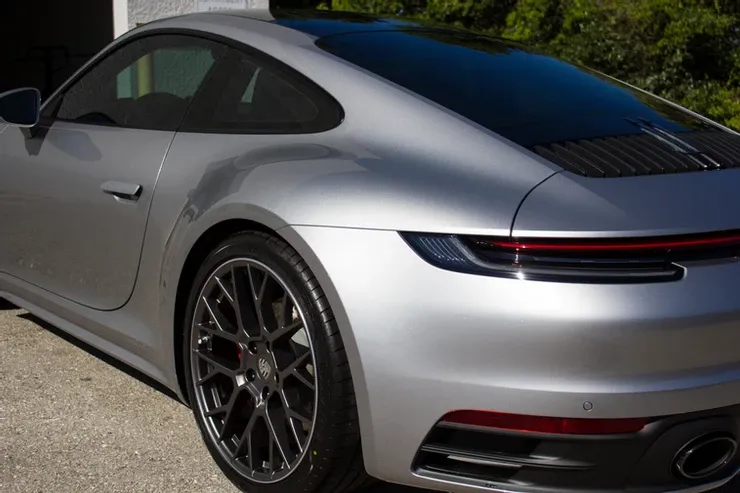 A silver porsche 911 is parked in front of a garage