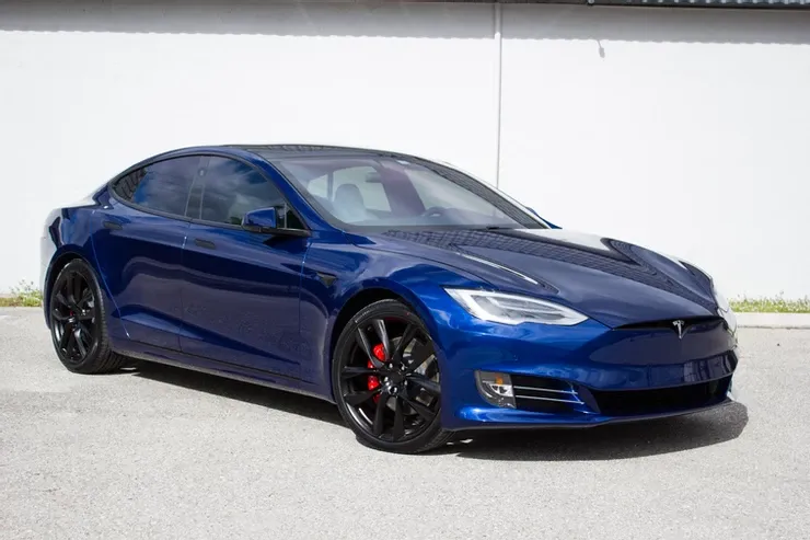 A blue tesla model s is parked in front of a white building.