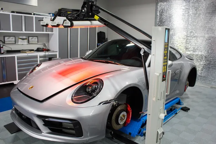 A silver porsche is sitting on a lift in a garage.