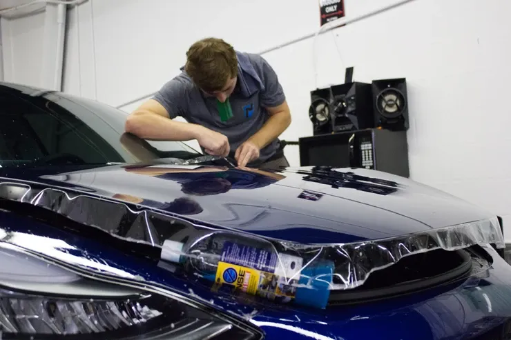 A man is working on the hood of a blue car.