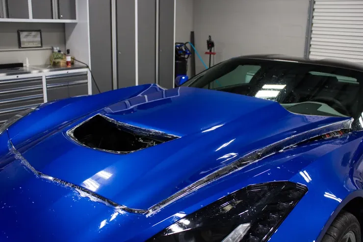 A blue sports car with the hood open is parked in a garage.