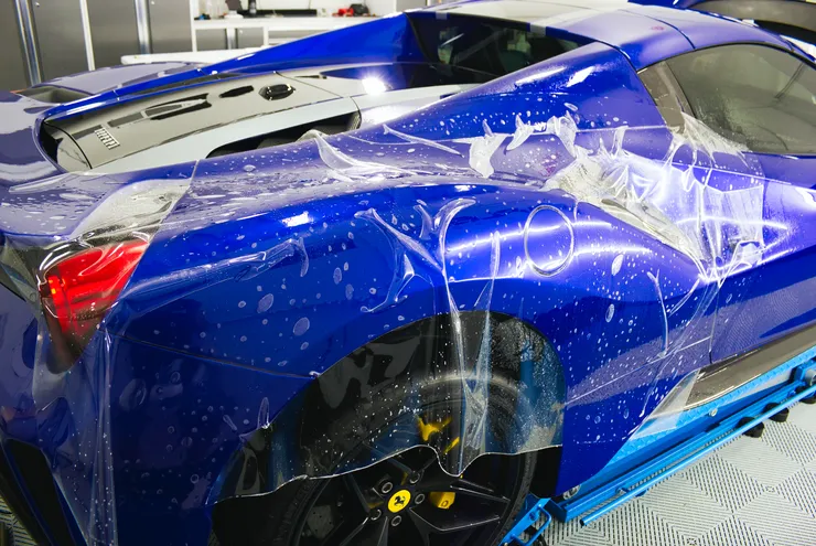 A blue sports car is covered in plastic wrap.