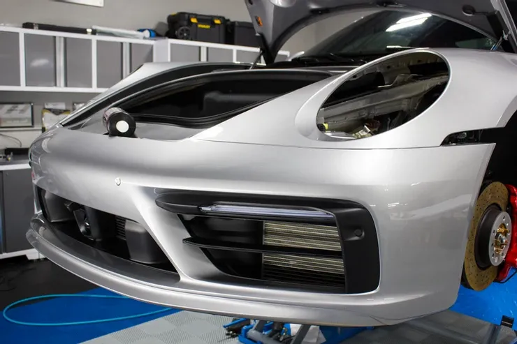 A silver sports car with the hood open is sitting on a lift in a garage.
