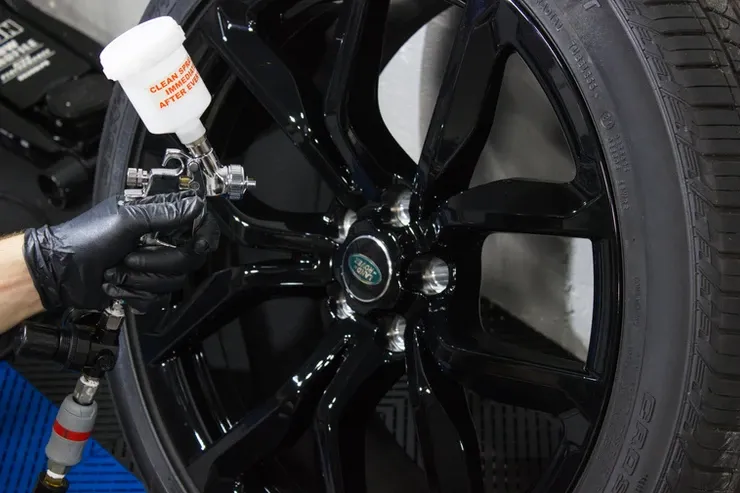 A person is spraying paint on a black wheel.