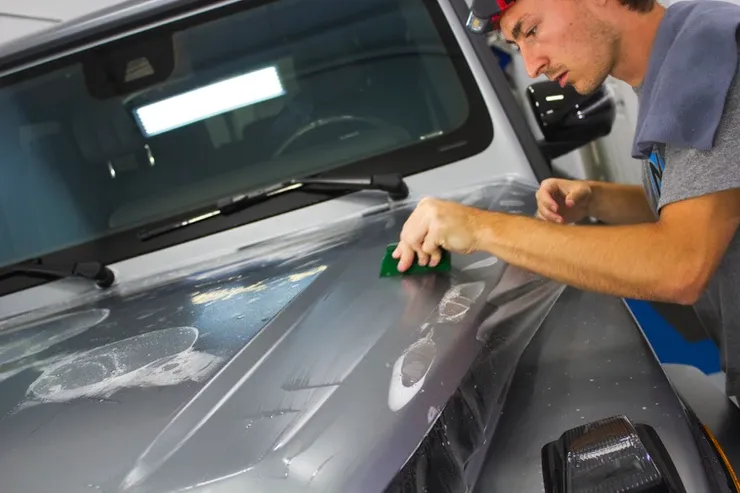 A man is wrapping the hood of a car with a plastic wrap.