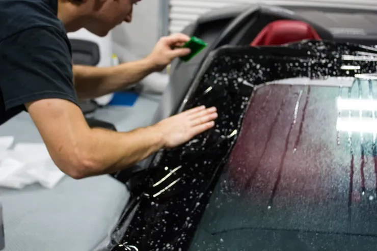 A man is cleaning the windshield of a car with a sponge.