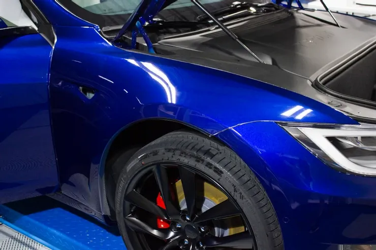 A blue tesla model 3 is sitting on a lift with the hood up.