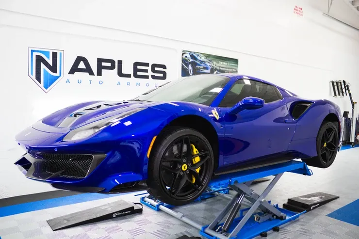 A blue ferrari is sitting on a lift in a garage.
