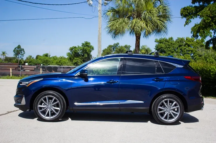 A blue suv is parked in a parking lot next to a palm tree.