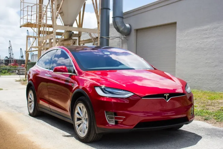 A red tesla model x is parked in front of a building.