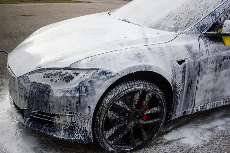 A tesla model s is covered in foam while being washed.