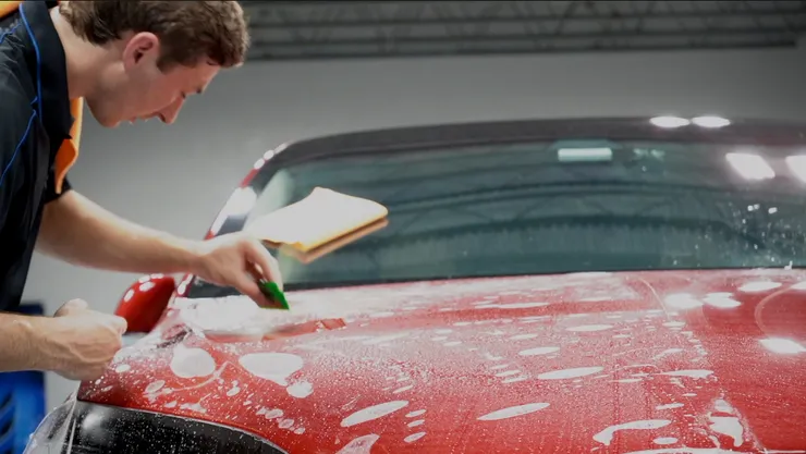A man is applying a protective film to the hood of a red car.