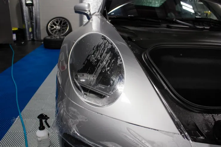 A silver car is covered in plastic wrap in a garage.