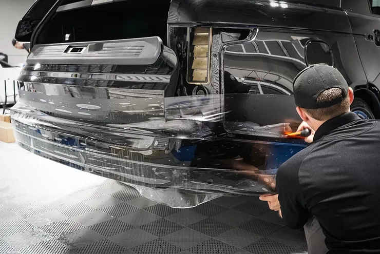 A man is wrapping the bumper of a car with plastic wrap.