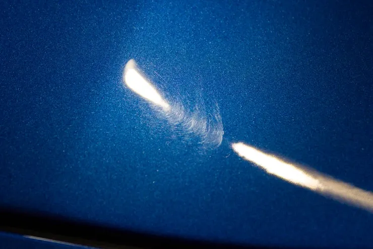 A close up of a blue car with a scratch on it.