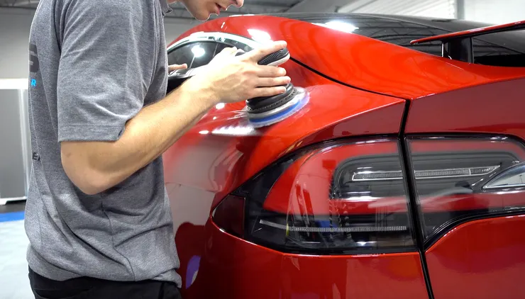 A man is polishing a red car with a sander.