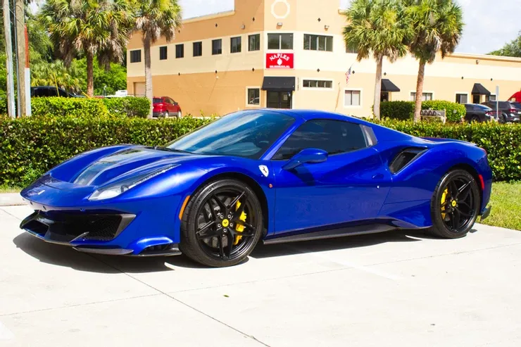 A blue ferrari 488 pista is parked in front of a building.