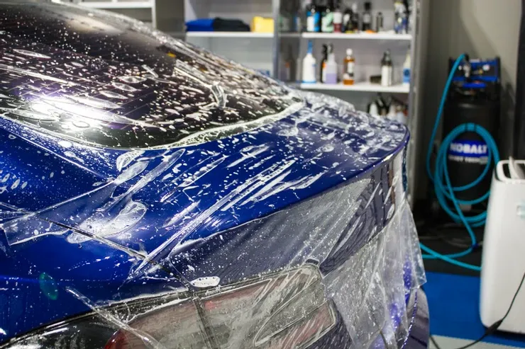 A blue car is wrapped in plastic in a garage.