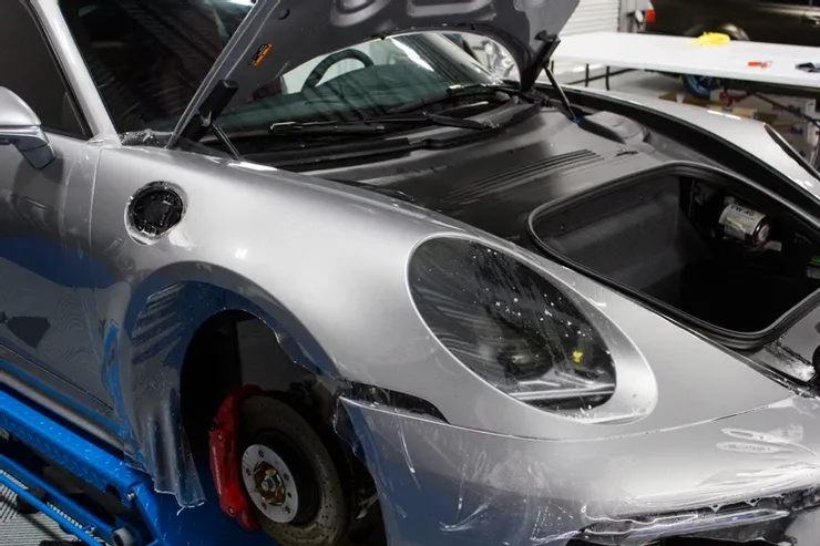 A silver porsche 911 is sitting on a lift with its hood open.