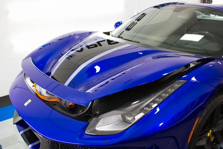 A blue sports car with the hood up is parked in a garage.