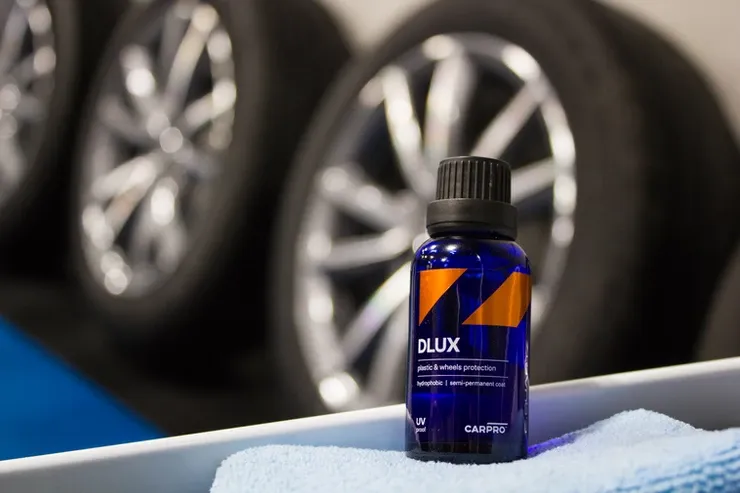 A bottle of polish is sitting on a towel next to a car wheel.