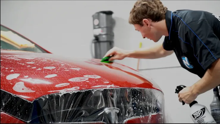 A man is cleaning a red car with a spray bottle