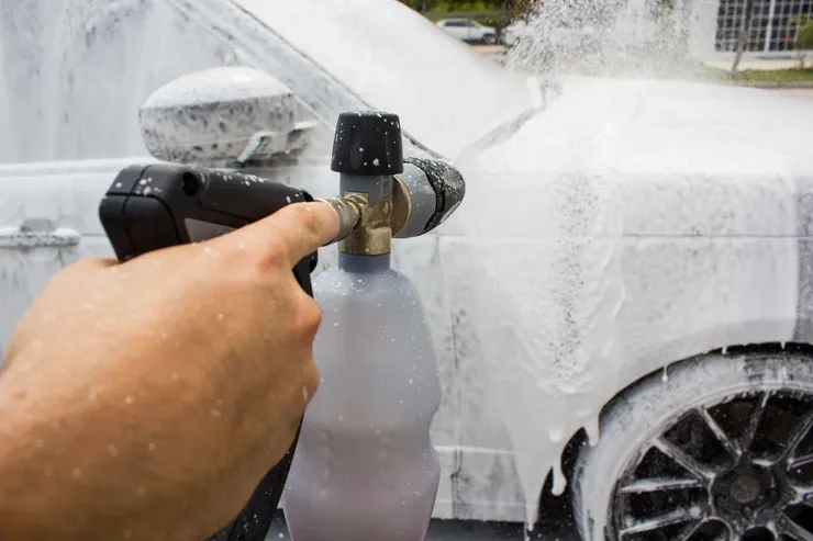 A person is spraying foam on a car with a high pressure washer.