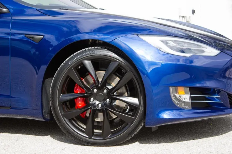 A close up of a blue tesla model s with black wheels and red brake calipers.