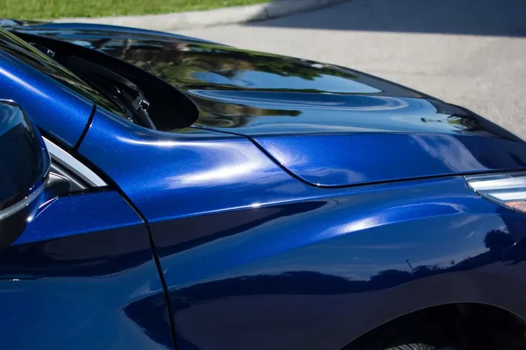 A blue car with a black hood is parked on the side of the road.