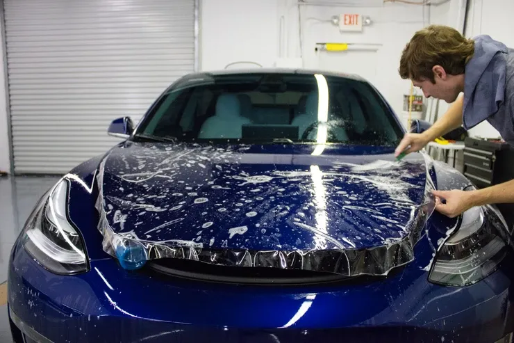 A man is applying a protective film to the hood of a tesla model 3.