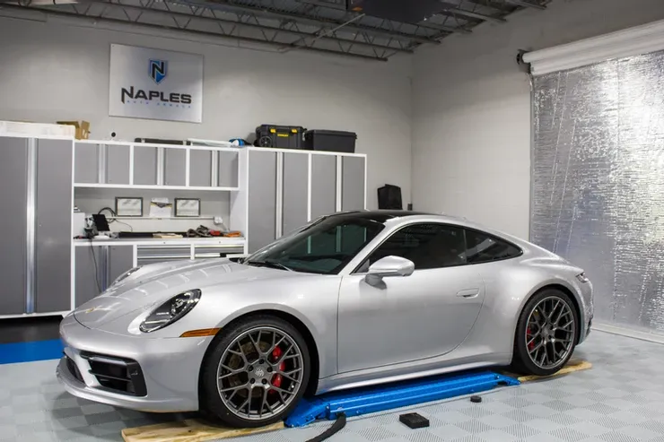 A silver porsche 911 is parked on a lift in a garage.
