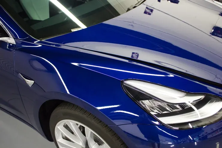 A blue car is parked in a garage with the hood up
