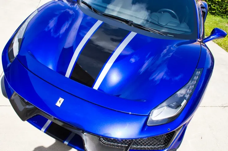 A blue sports car with white stripes on the hood is parked on the side of the road.